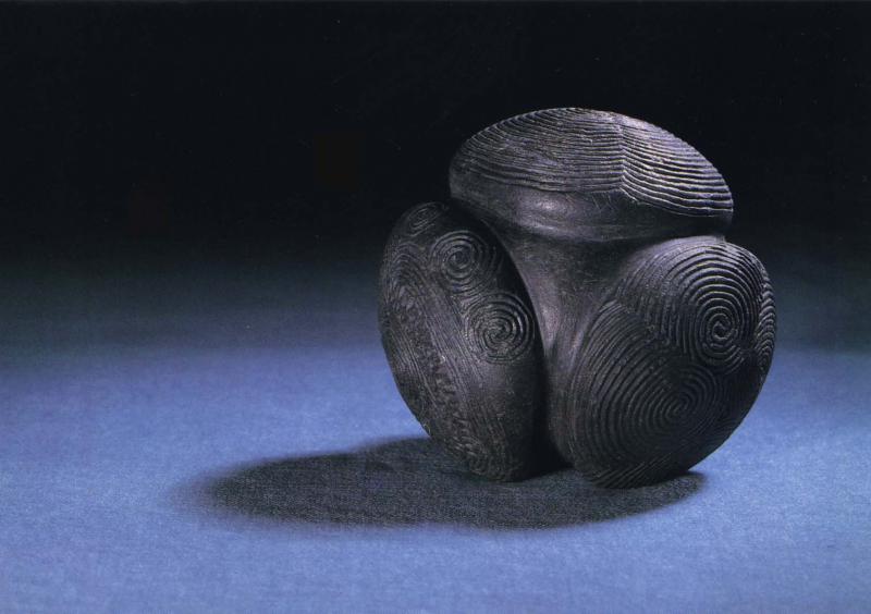 A photograph of a carved black stone ball with protruding surfaces each decorated with a different swirling decoration from Towie in Aberdeenshire